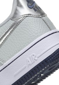 Gros plan du talon d'une basket Nike Air blanche et argentée avec cuir texturé et semelle noire visible.