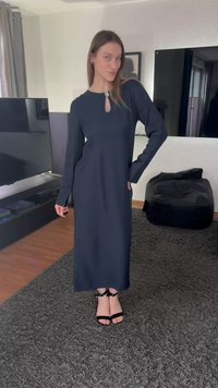 Lang navyblå kjole med lange ærmer, et nøglehul i halsudskæringen, glat tekstur, og kombineret med sorte hæle med stropper på et tekstureret tæppe.