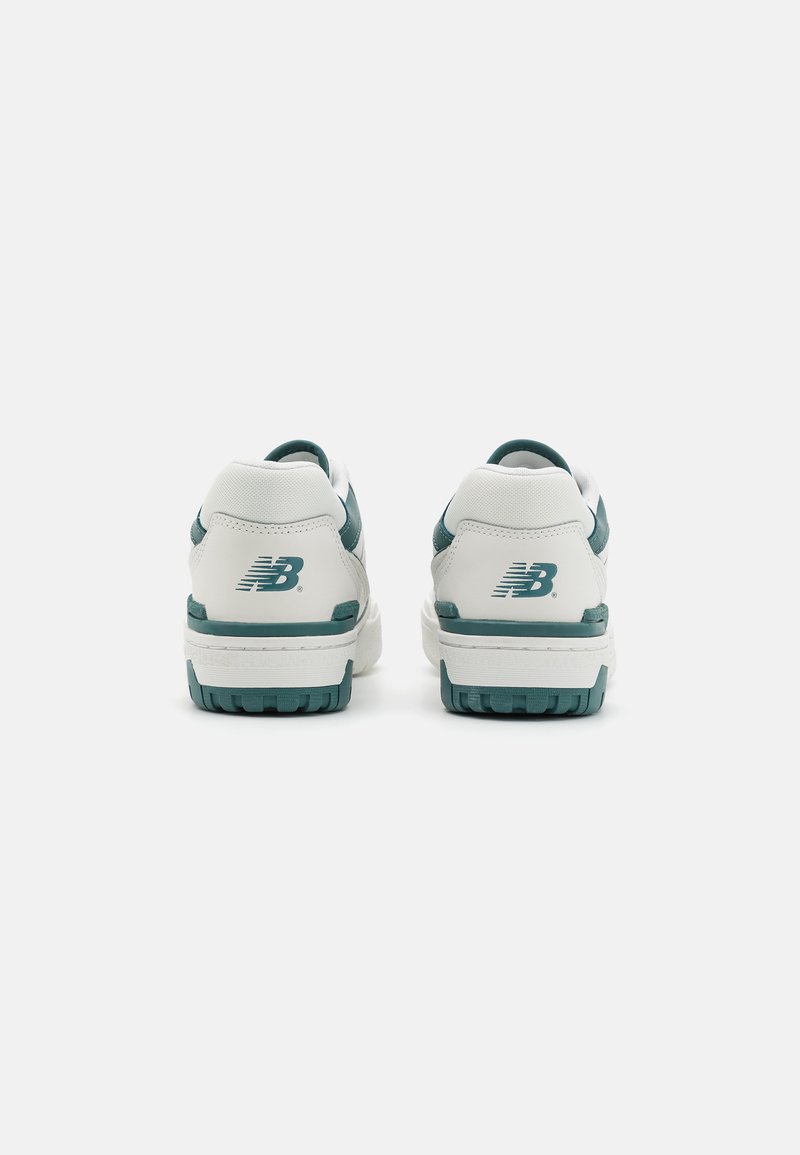 Des sneakers blancs avec des accents teal, dotés d'une tige en cuir lisse, d'un col rembourré et d'une semelle en caoutchouc texturée. Logo visible sur le talon.
