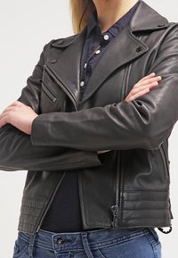 Black leather biker jacket with zippered pockets, snap collar, and quilted shoulder details. Worn over a navy button-up shirt.