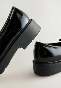 Pantofi din piele patent neagră cu o finisare lucioasă, având o talpă groasă din cauciuc negru și un design cu vârf rotund.