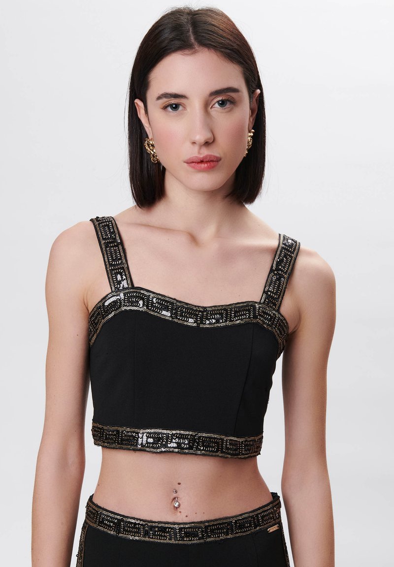 Zwarte cropped top met ingewikkelde gouden kralenbanden en tooi. Heeft een aansluitend ontwerp en een zachte textuur.