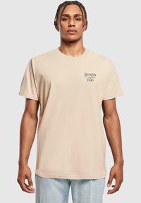 Beige cotton t-shirt with a relaxed fit, round neckline, and short sleeves. Features "Sunday Coffee Run" text graphic on the left chest.