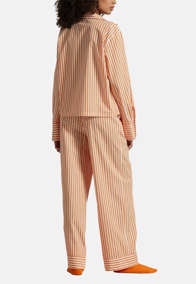 Pomarańczowo-biały piżama w paski, z koszulą na kołnierzyk i długimi rękawami, w komplecie z dopasowanymi luźnymi spodniami i pomarańczowymi skarpetami.