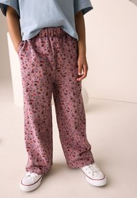 Pantaloni rosa a fiori con una fascia elastica in vita, caratterizzati da un motivo strutturato di piccoli fiori rossi e blu, abbinati a scarpe da ginnastica bianche.