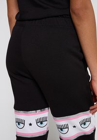 Svarta joggers med en glänsande midja och ögon grafiktryck i rosa, vitt och blått på de nedre benen. Mjuk, elastisk tyg.