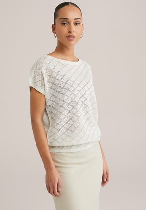 White knitted sweater with a diamond pattern, short sleeves, and a relaxed fit, paired with a light beige pencil skirt.