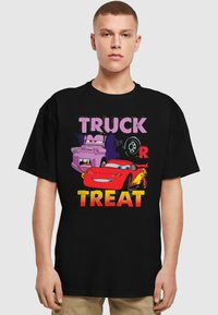 Must venitus musta T-särk, millel on koomiksite autod ja julge tekst "TRUCK OR TREAT" erkkollastes värvides. Kangelased on lilla veok ja punane auto.