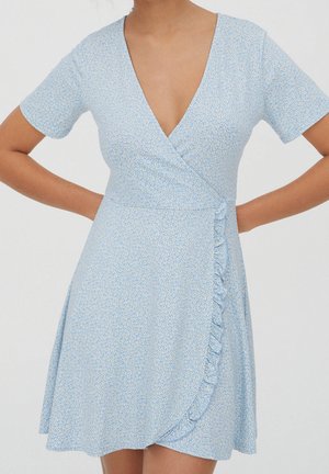 Robe portefeuille bleu clair avec petit motif floral blanc, manches courtes, encolure en V, et détail à volants sur le côté droit devant.