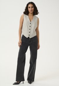 Gilet gris clair à rayures, avec un col en V, cinq boutons noirs et un ourlet ajusté, associé à un pantalon noir ample et des chaussures pointues noires.