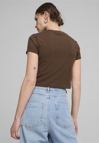 Brun cropped t-shirt med korte ærmer, parret med højden blå denim jeans med to baglommer og en falmet tekstur.