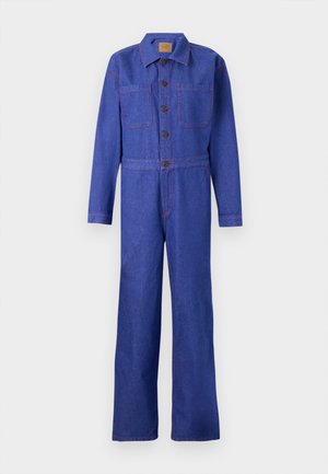 Salopette en denim bleu vif à manches longues, avec de grandes poches avant et des coutures contrastantes rouges. Elle dispose d'une fermeture à boutons sur le devant et de jambes larges.
