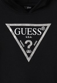 Czarna bluza z kapturem z logo w srebrnym brokacie w kształcie trójkąta z tekstem "GUESS U.S.A. WASHED JEANS" oraz wzorem znaku zapytania na środku.