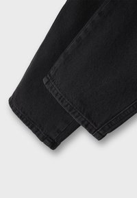 Podrobnosti črnih jeansa iz jeansa, ki prikazujejo rob z ravnim robom in vidnimi šivi, poudarjajoč teksturo in težo tkanine.