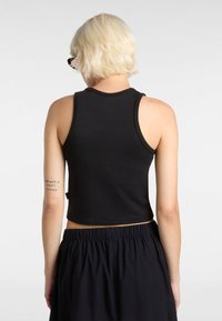 Black cropped tank top with sleeveless design. Features a round neckline and minimal stitching. The model wears black, elastic-waist shorts.