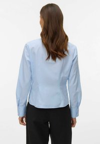 Jasnoniebieska bluzka z długim rękawem o dopasowanym kroju, z mankietami na guziki i gładką fakturą; widok z tyłu ukazuje czystą, dopasowaną sylwetkę.