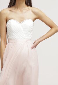 Robe de soirée sans bretelles avec un corsage blanc texturé agrémenté de sequins et une jupe en tulle rose fluide, cintrée à la taille.