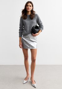 Maglione in lana grigia, mini gonna argento metallizzato, borsa nera strutturata e décolleté argentate lucide a punta. Dettagli di design semplici e moderni.