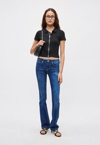 Czarna krótka koszulka polo z przednim zamkiem błyskawicznym, w połączeniu z niebieskimi dżinsami o prostych nogawkach, małą czarną torebką i czarnymi sandałami.