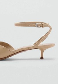Sandales à talons beiges au design minimaliste, avec une tige en cuir lisse et mat, une fine bride à la cheville et un talon court et effilé.