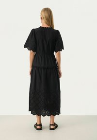 Rochie din bumbac neagră cu mâneci scurte, bufante, talie ajustată și o fustă în mai multe straturi, având un tiv dantelat și modele în formă de diamant decupate.