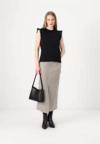 Svart ärmlös topp med volangaxlar, kombinerad med en randig midikjol. Modellen håller en liten svart handväska och har på sig svarta stövlar som går upp till knäna.