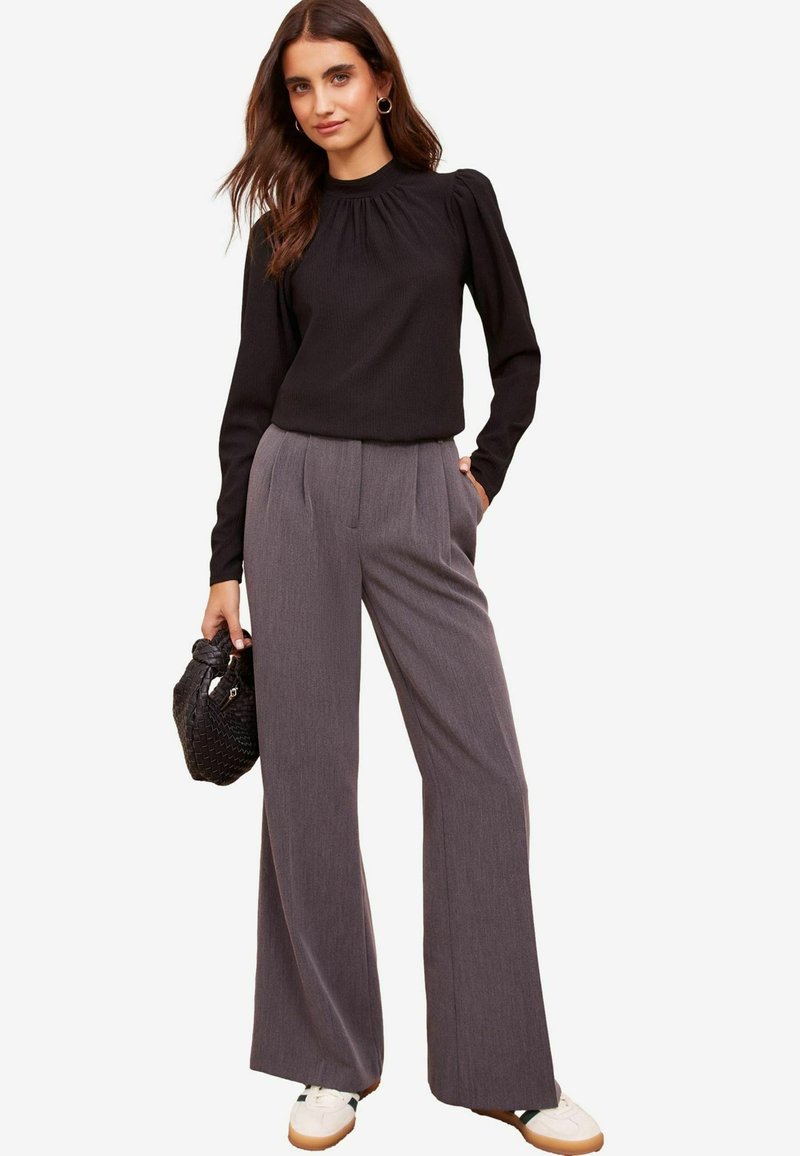 Top a maniche lunghe nera a costine con scollo arricciato, abbinato a pantaloni larghi grigi chiari. Borsa nera testurizzata e sneakers bianche.