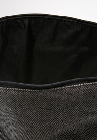 Borsa con motivo a spina di pesce nero, dotata di una zip sulla parte superiore, che rivela un interno liscio e semplice di colore nero e bordi rinforzati per una maggiore durabilità.