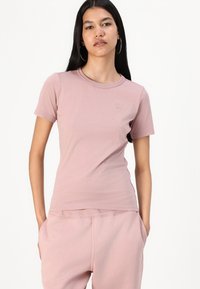 Camiseta corta de manga corta en color rosa claro, con cuello redondo y un pequeño logo en el pecho. Textura suave y lisa, y diseño ajustado.