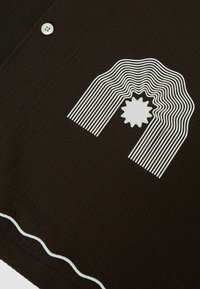 Tissu noir texturé avec une étoile blanche brodée à l'intérieur d'un motif arc-en-ciel rayé et un bouton blanc près du coin supérieur gauche.