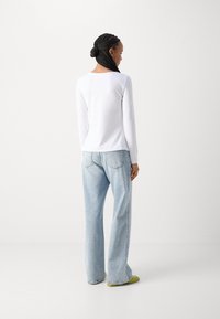 Long-sleeved white shirt, paired with light blue wide-leg jeans and green shoes. Simple design with a comfortable fit.