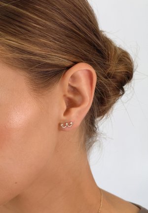 Silver ear cuff featuring a wave design with three curved accents, adorned with small clear gemstones. Styled on a model's ear.