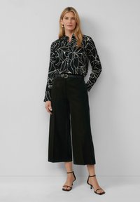 Zwarte blouse met wit bladpatroon, met kraagontwerp, gecombineerd met zwarte wijde broek en zwarte strappy heels. Soepele texturen.
