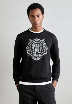 Black sweatshirt with a textured white tiger graphic on the front, featuring a round neck and ribbed cuffs. Worn over a white shirt.