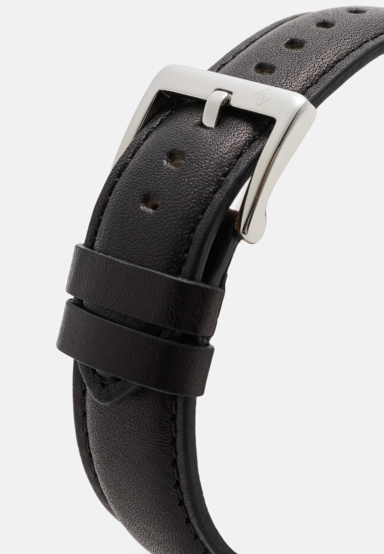 Svart läderarmband med perforerat mönster, silvermetallspänne och två hållare. Strukturerad yta och snyggt stygnsynligt.