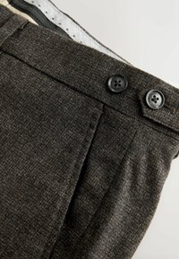 Dark fabric trousers featuring a textured weave, two black buttons at the waist, and a pleat detail on the front.