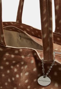 Ruskea tekokarvahandbag, jossa on valkoinen pilkullinen kuvio, vetoketjukiinnitys, sisätasku ja metallilappu, johon on kaiverrettu "Stradivarius".
