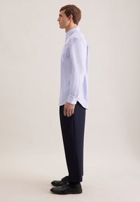 Camicia a maniche lunghe azzurro chiaro con una texture sottile e due tasche sul petto, abbinata a pantaloni blu scuro e scarpe nere.