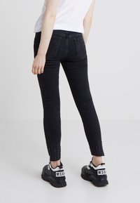Black skinny jeans with a mid-rise waist, featuring textured cutouts at the ankle. Paired with chunky black sneakers with white accents.