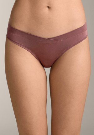 Weiblicher Oberkörper, der nahtlose Baumwollunterwäsche in Mauve mit einem V-förmigen Bund vor neutralem Hintergrund trägt.