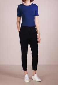 Top corto de manga corta azul combinado con pantalones negros ajustados con rayas laterales grises, usado con zapatillas blancas. Textura de tela suave.