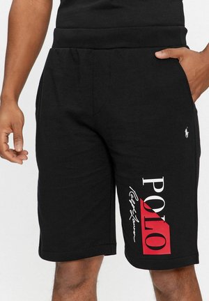 Pantaloncini neri con il logo "POLO Ralph Lauren" rosso e bianco sulla gamba destra, indossati da una persona con una mano in tasca e una mano rilassata.