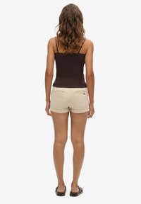 Bruine tanktop met kantdetails, gecombineerd met lichtbeige denimshorts. De shorts hebben achterzakken en opgerolde mouwen.
