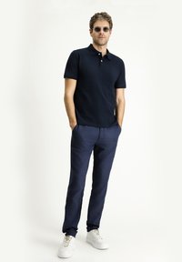 Polo blu, pantaloni blu e sneakers bianchi. La maglietta ha un colletto e maniche corte; i pantaloni hanno una finitura texturizzata.