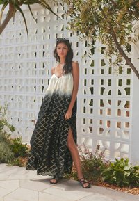 Robe maxi noir et crème avec un design dégradé, dotée de fines bretelles et d'une fente sur le côté. Le tissu a une texture à motifs.