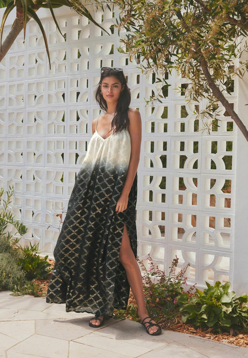 Robe maxi noir et crème avec un design dégradé, dotée de fines bretelles et d'une fente sur le côté. Le tissu a une texture à motifs.