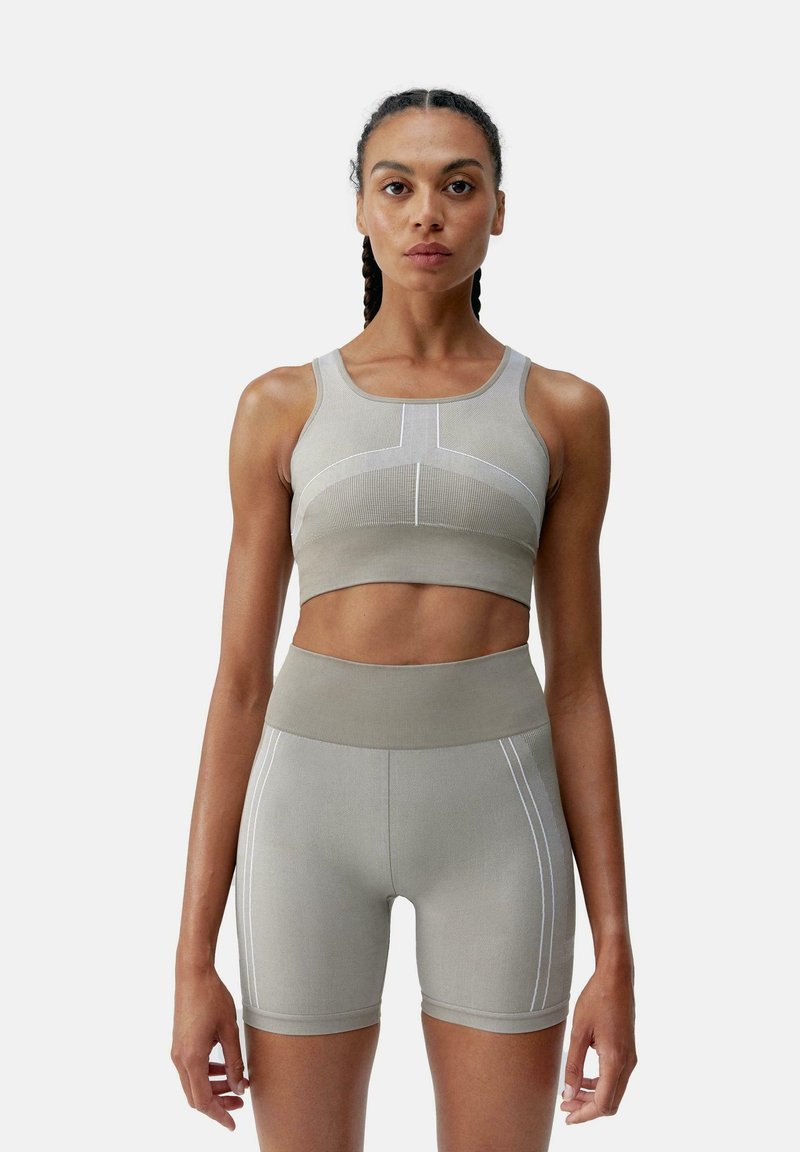 Reggiseno sportivo grigio chiaro e pantaloni corti a vita alta coordinati, caratterizzati da una trama a coste e linee di accento bianche. Design aderente per il massimo comfort.