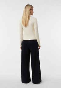 Kremowa bluzka z długim rękawem w połączeniu z czarnymi szerokimi spodniami. Gładka tkanina, dopasowany krój bluzki, luźny fason spodni. Prosty design.