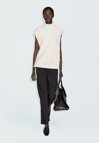 Lichtroze mouwloos gebreid topje met hoge hals, gecombineerd met zwarte losse trousers en een gestructureerde zwarte handtas. Eenvoudig, modern ontwerp.