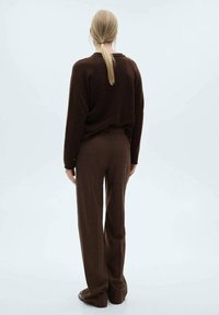 Hnědý pletený svetr a hnědé kostkované kalhoty nošené dohromady; měkká textura, volný střih, dlouhé rukávy a neformální design. Vlasy svázané do culíku.